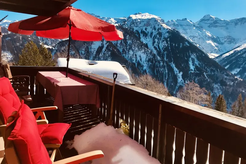 The balcony with a red parasol and chairs, snowy mountains beyond