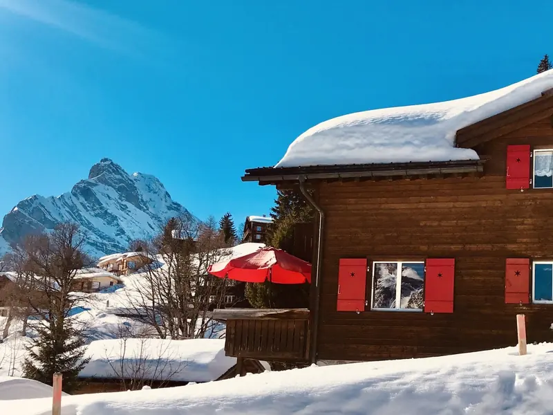 Chalet Heidi in the snow, with red shutters and a red parasol