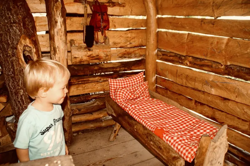 Inside a log hut with a little bed in red check