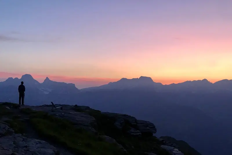 A pink sky over the ridges, a figure on a rocky edge