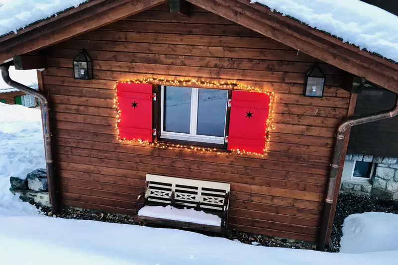 Red shutters with fairy lights and a bench in the snow