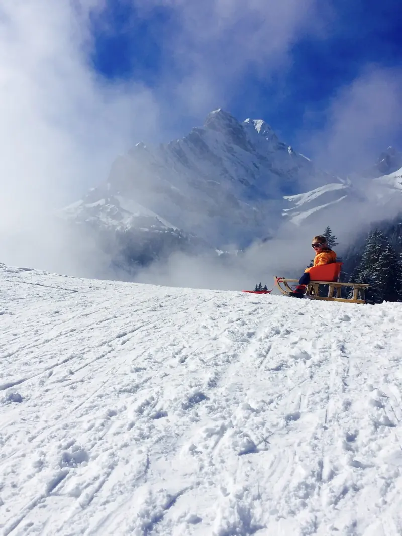A child on a wooden sledge, mountains above the clouds