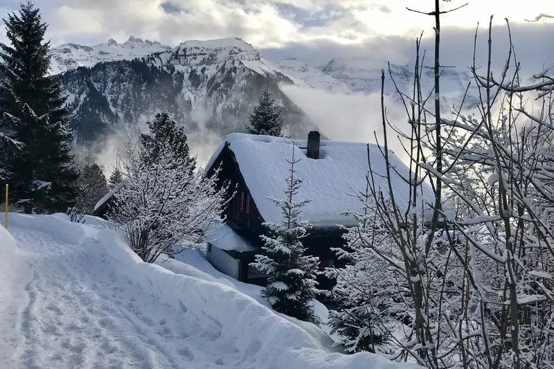 A snowy path past a chalet, mountains in the clouds